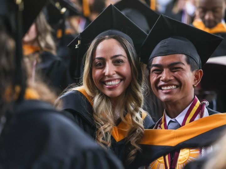 在毕业典礼上，两名学生戴着帽子，穿着长袍摆姿势拍照
